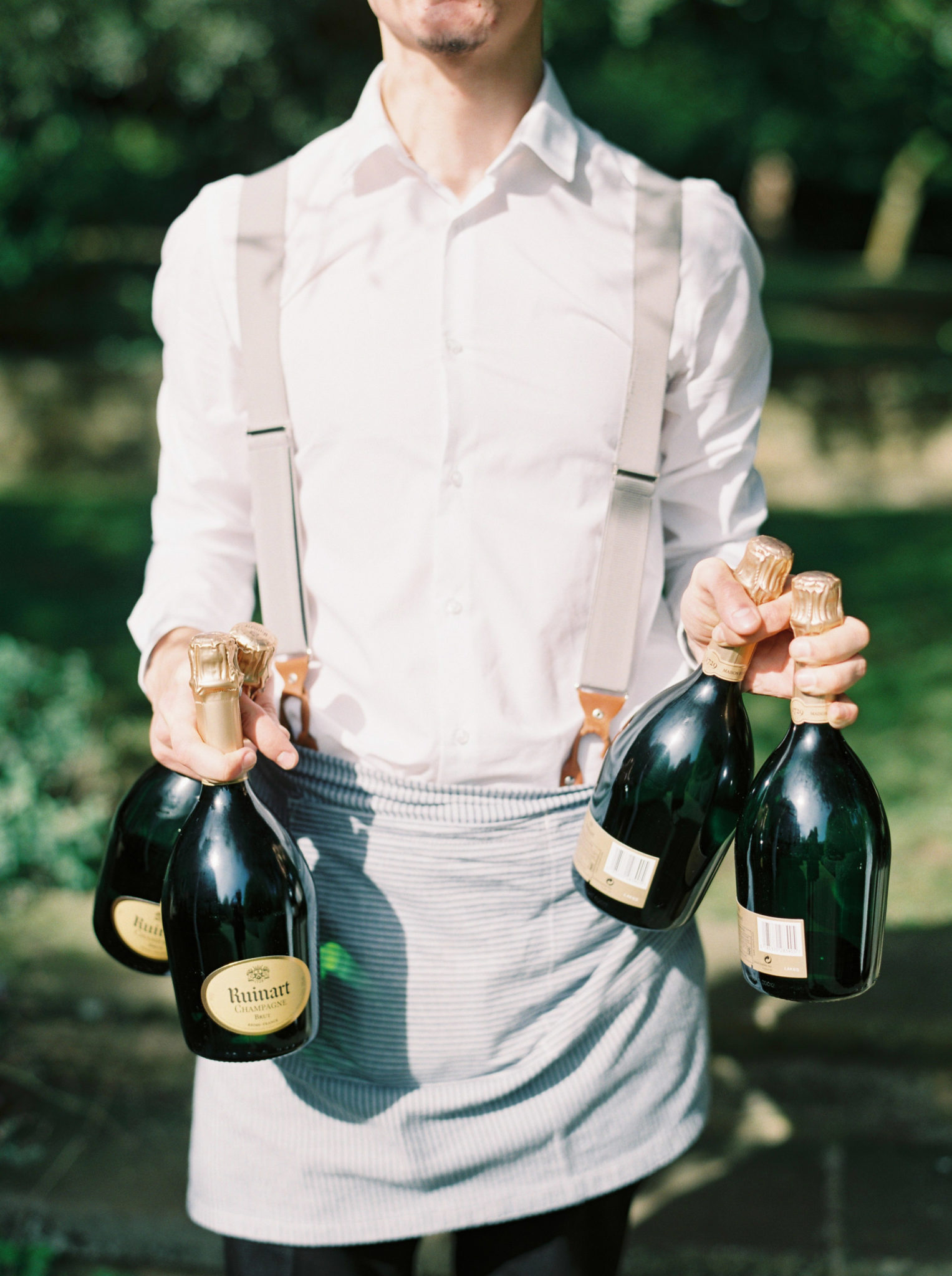 Barman carrying champagne bottles at an outdoor wedding reception.